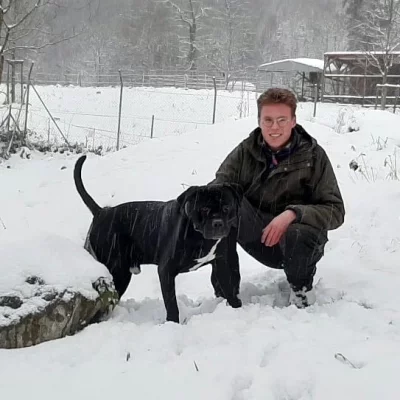 Ein schwarzer Hund, neben ihm kniet ein Mann im Schnee